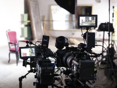 Zwei professionelle Videokameras auf Stativen in einem hellen Studio filmen einen einzelnen, roten, gepolsterten Stuhl